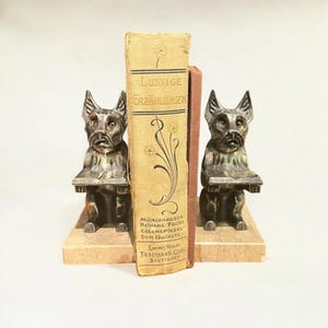 A pair of Art Deco bookends made of silver pewter - reading Scotch Terriers on marble platters with compact dimensions.