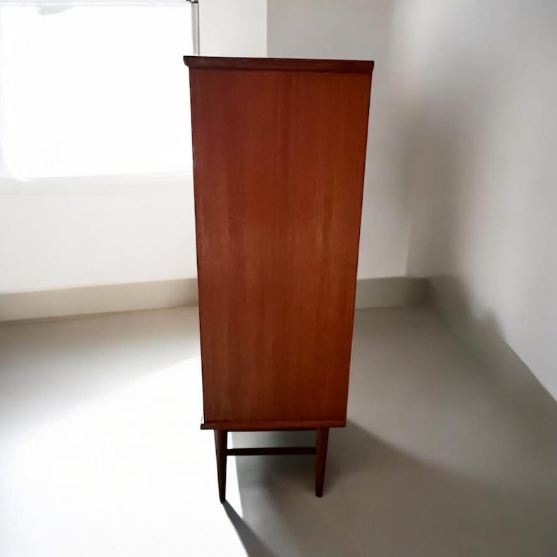 Puede incluir: Un armario de madera alto con un acabado marr&oacute;n claro. El armario tiene cuatro cajones y dos puertas. El armario est&aacute; de pie sobre cuatro patas.
