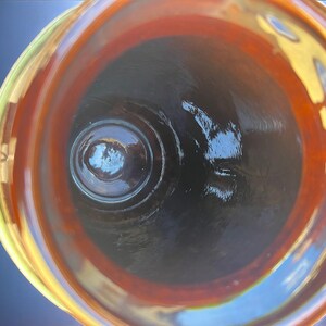 May include: An overhead view of a glass vessel with a wide, swirling rim. The rim transitions from yellow to orange, framing a dark interior. The glass has a glossy finish, reflecting light and creating a sense of depth. The vessel's design suggests it could be a decorative bowl or vase.