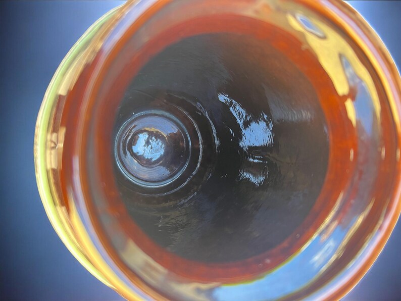 May include: An overhead view of a glass vessel with a wide, swirling rim. The rim transitions from yellow to orange, framing a dark interior. The glass has a glossy finish, reflecting light and creating a sense of depth. The vessel's design suggests it could be a decorative bowl or vase.