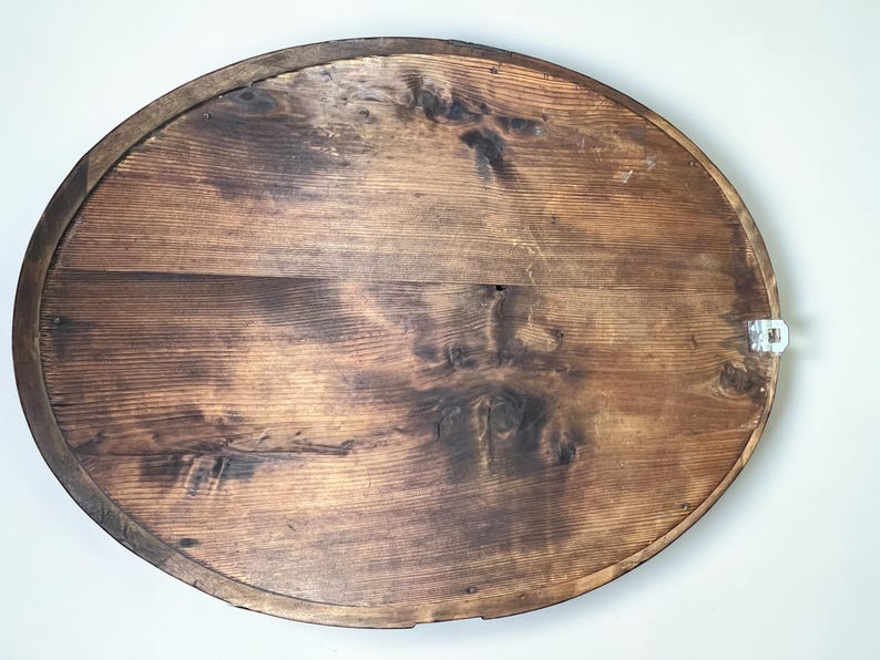 May include: Oval wooden wall art with a dark brown finish. The back of the piece shows the wood grain and a metal hanger. The wood has a distressed look with knots and variations in color.