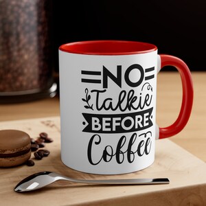 Puede incluir: Taza de café blanca con borde y asa rojos. La taza tiene texto negro que dice "NO Talkie Before Coffee".