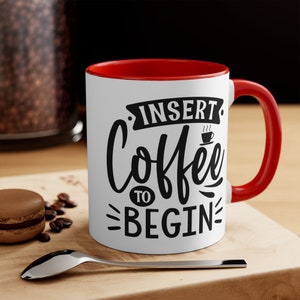Puede incluir: Taza de café blanca con borde y asa rojos. La taza tiene texto negro que dice "Insert Coffee to Begin".