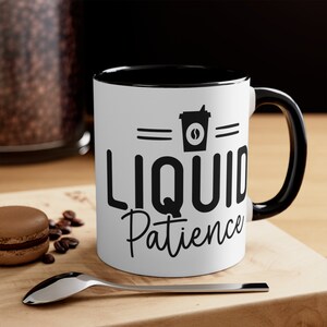 Puede incluir: Taza de café blanca con borde y asa negros. La taza tiene un gráfico negro de una taza de café con el texto "Liquid Patience" en ella.