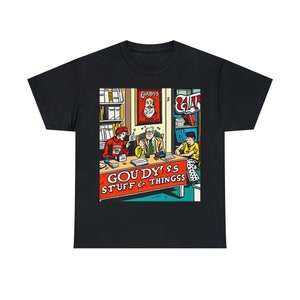 May include: A black t-shirt with a colorful illustration of a comic book store called "Goudy's Stuff & Things". The illustration features three people sitting at a table with books and other items. The store has a sign above the door that says "Goudy's".