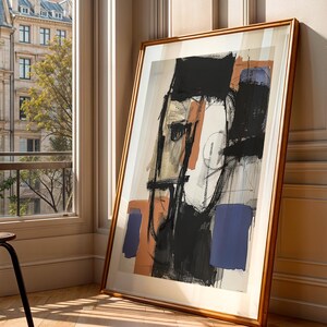 May include: An abstract artwork in a wooden frame leans against a wall. The art features a face-like composition with black, orange, and blue shapes on a white background. A black chair with a woven seat sits near a window overlooking a city.