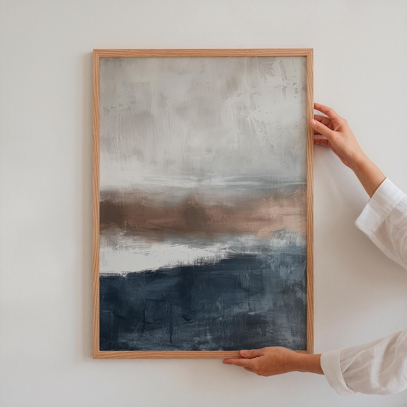 May include: Abstract landscape painting in a light wooden frame. The artwork features a layered composition of muted colors, including shades of gray, brown, and deep blue. The brushstrokes create a textured effect, evoking a sense of depth and atmosphere.