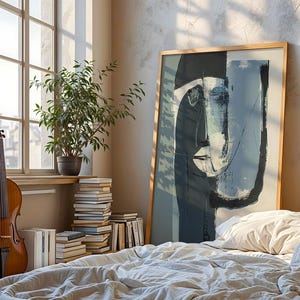 May include: A cello stands near a window with a stack of books and a potted plant. A large framed abstract art piece leans against a bed with a white comforter. The artwork features a face in shades of blue and gray.