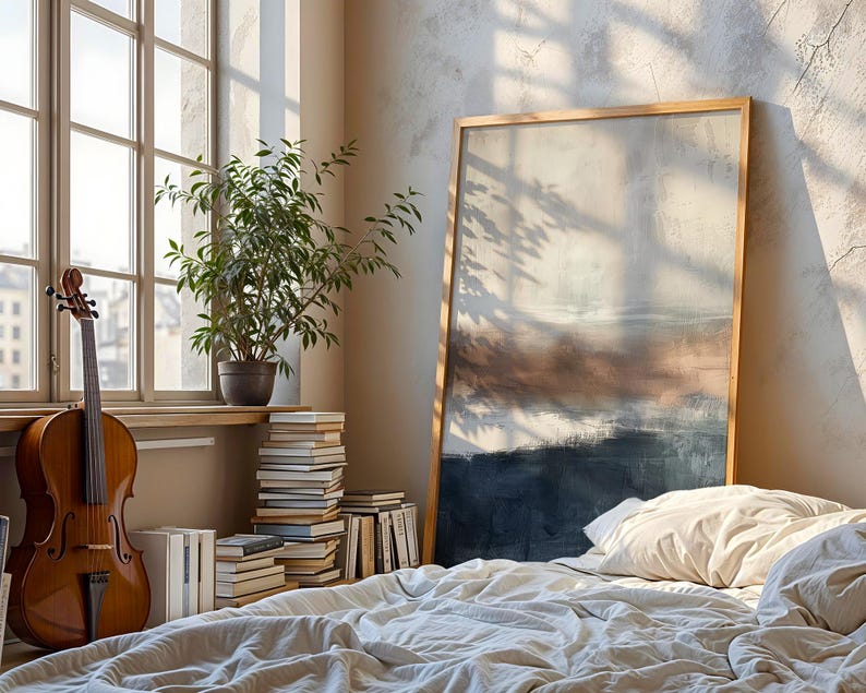 May include: A cello leans against a window with sunlight streaming through. A large framed abstract painting rests against the wall near a bed with white linens. A potted plant and stacked books are also visible.