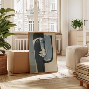 May include: Abstract art print featuring a stylized face in shades of blue, black, and white, framed in natural wood. The artwork leans against a neutral-toned wall, adding a touch of modern art to the interior decor.