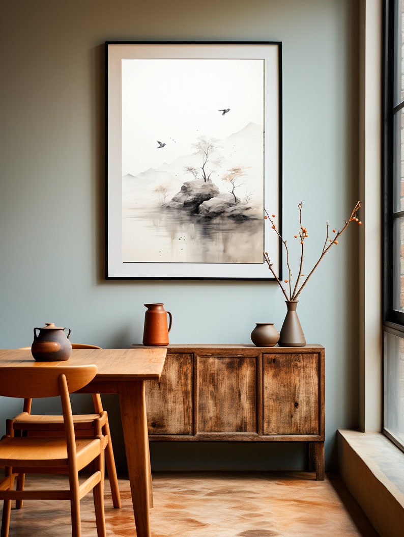 May include: A framed watercolor painting of a small island with trees and birds in a misty landscape. The painting is hanging on a light green wall above a wooden cabinet with two chairs and a table in front of it.