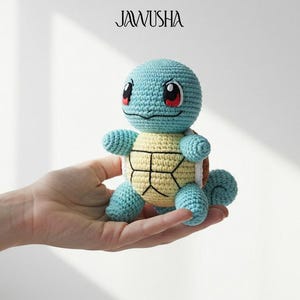 May include: A crocheted Squirtle plush toy in shades of blue, yellow, and tan. The handmade toy features a round head, small arms and legs, and a shell-like pattern on its belly. The toy is held in a hand.