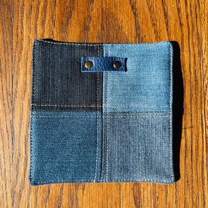 Peut inclure: Un dessous de verre en denim bleu et noir avec une sangle en cuir et deux rivets en laiton. Le dessous de verre est composé de quatre carrés de denim cousus ensemble.