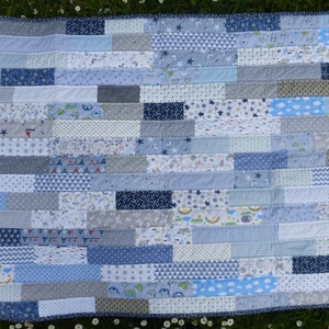 Könnte beinhalten: Eine Patchwork-Babydecke mit verschiedenen blauen, weißen und grauen Stoffen. Die Decke besteht aus horizontalen Stoffstreifen mit unterschiedlichen Mustern, darunter Sterne, Streifen und geometrische Formen.