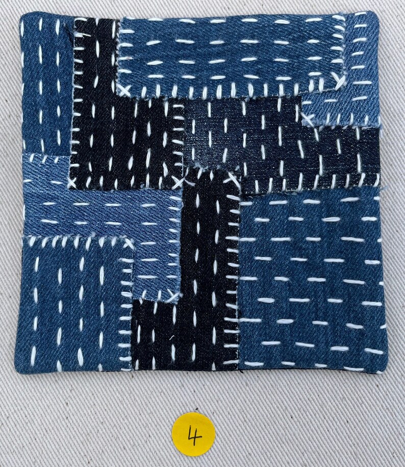 May include: A blue and black patchwork square made of denim fabric with white stitching. The square is numbered "4" in yellow.