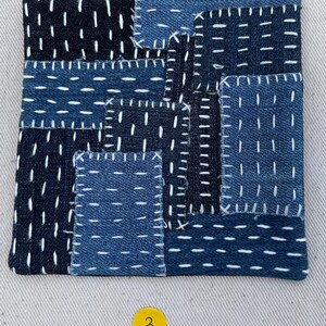 May include: A patchwork quilt made of blue denim fabric with white stitching. The quilt is made up of many small squares and rectangles, and the stitching is done in a variety of patterns. The quilt is numbered "3" in the bottom right corner.