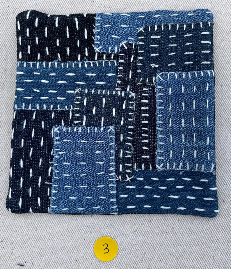 May include: A patchwork quilt made of blue denim fabric with white stitching. The quilt is made up of many small squares and rectangles, and the stitching is done in a variety of patterns. The quilt is numbered "3" in the bottom right corner.