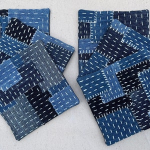 Op de afbeelding: Set van zes blauwe en zwarte denim onderzetters met witte stiksels. De onderzetters zijn gemaakt van patchwork stof en zijn gerangschikt in twee stapels van drie.