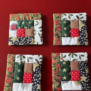 Puede incluir: Cuatro posavasos acolchados hechos a mano con un diseño de patchwork en telas rojas, verdes, blancas y azules. Los posavasos tienen un tema navideño con acebo, estrellas y lunares.