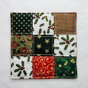 Peut inclure: Un dessous de plat en tissu patchwork vert et rouge sur le thème de Noël. Le dessous de plat est composé de neuf carrés de tissus différents, chacun avec un motif différent. Les motifs comprennent des feuilles de houx, des étoiles, des pois et des motifs floraux.
