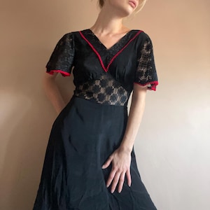 Könnte beinhalten: Ein schwarzes Maxikleid mit einem Spitzenoberteil und roten Verzierungen. Das Kleid hat einen V-Ausschnitt und kurze Ärmel.
