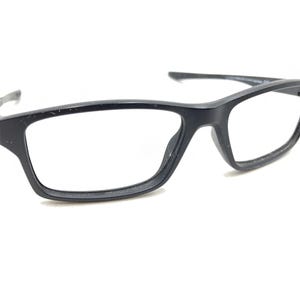 May include: Black rectangular eyeglasses with clear lenses. The glasses have a matte finish and a modern design. The frames are thick and sturdy, suitable for everyday wear. The temples curve slightly for a comfortable fit.