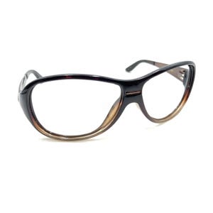 May include: Eyeglasses with a dark brown, tortoise-shell patterned frame. The frames feature a rounded, wide shape with a distinct bridge connecting the two lenses. The temples are thin and dark, extending from the outer edges of the frame.