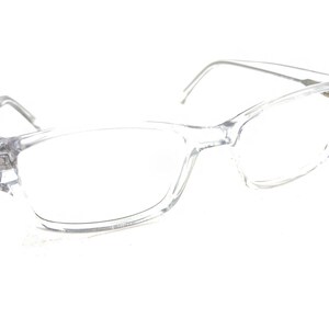 Puede incluir: Gafas rectangulares transparentes con montura transparente y finas varillas plateadas. Las gafas tienen un diseño clásico, adecuado para el uso diario. Las lentes son claras y la estética general es moderna y minimalista.