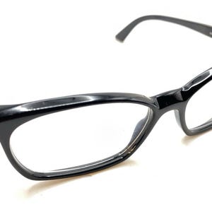 May include: Black spectacles with a glossy finish, featuring a classic rectangular frame shape and thin temples. The glasses have clear lenses and a small metallic detail on the outer hinge area, providing a clean and functional design for vision correction.