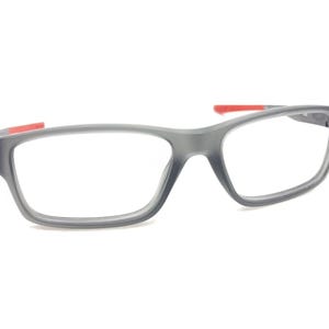 May include: Gray eyeglasses with red accents on the arms. The frame has a rectangular shape with a slightly curved top.