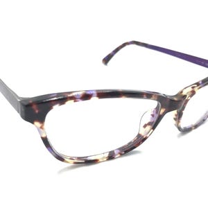 May include: Cat-eye glasses featuring a tortoiseshell frame with blended brown, black, and purple tones. The temples are solid purple on the interior, and the frame has a glossy finish with clear lenses. The design includes integrated nose pads.