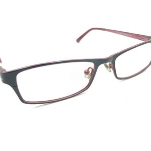 Pode incluir: Óculos retangulares com armação cinza escuro e detalhes bordô. As lentes são transparentes e as hastes são finas. Os óculos têm um design moderno e minimalista, adequados para o uso diário.