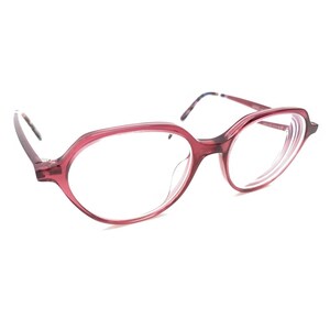 May include: Translucent deep red eyeglasses featuring a rounded, slightly angular frame shape. The temples are thin and feature a subtle multi-colored pattern on the inner side. The clear lenses are set within the glossy, semi-transparent red frame.