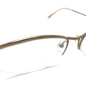 May include: Eyeglasses with a gold-coloured metal frame. The clear lenses are set in a delicate, curved frame. The thin temples extend to the ear pieces.