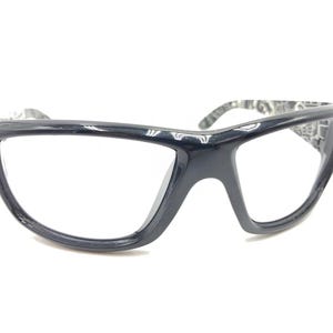 Puede incluir: Gafas de seguridad negras con lente transparente y montura negra. La montura tiene un diseño único con una forma curva.