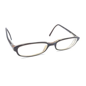 May include: A pair of eyeglasses featuring dark brown rectangular frames with a contrasting light beige inner rim. The glasses have thin, dark brown temples and clear lenses, presented in a three-quarter view against a plain white background.