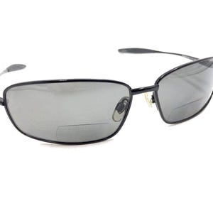 Könnte beinhalten: Schwarze rechteckige Sonnenbrille mit dunkelgrauen Gläsern. Die Sonnenbrille hat einen dünnen Metallrahmen.