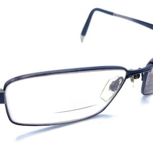 Könnte beinhalten: Eine Brille mit einem dunkelblauen Metallrahmen. Die rechteckigen Gläser sind klar, und die Bügel haben ein gestreiftes Design. Die Brille ist vor einem weißen Hintergrund platziert.