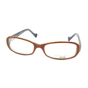 Op de afbeelding: Ovaalvormige bril met een glanzend bruin montuur en heldere glazen. De pootjes zijn donkergrijs met een opvallend gebogen uiteinde. Een kleine sticker op het rechterglas toont de tekst "POZZO DESIGN" en "195.00€" in zwarte en groene letters.