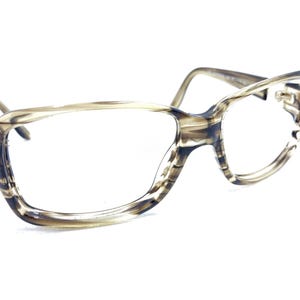 May include: A pair of eyeglasses with a light brown and dark brown marbled pattern. The frames have a cat-eye shape and clear lenses. The temples are a light brown color.