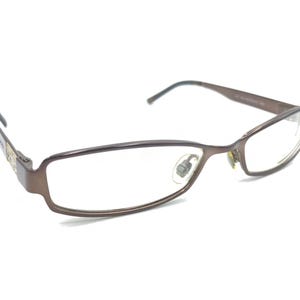May include: Brown rectangular eyeglasses with clear lenses. The frames are a muted brown colour, with a subtle metallic sheen. The temples are thin and curve gently to fit behind the ears. The glasses have a modern, minimalist design.