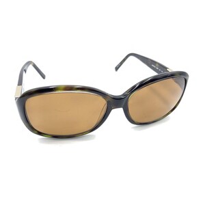 May include: Sunglasses with a dark tortoiseshell frame and brown lenses. The oval-shaped lenses are set in a sleek, curved frame. The temples are dark and slender, with a silver accent near the hinges. The sunglasses are designed for eye protection.