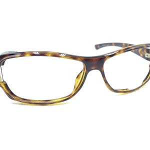 Puede incluir: Gafas de carey con un patrón marrón y amarillo. Las monturas tienen un diseño curvo y presentan detalles decorativos en las patillas. Las lentes son transparentes y las gafas están sobre un fondo blanco.