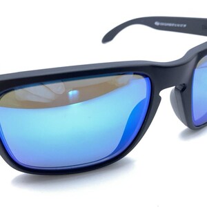 May include: Black sunglasses with blue mirrored lenses. The sunglasses have a square frame and a curved arm design. The lenses reflect a blue hue, and the frame has small silver accents near the hinges. The sunglasses are set against a white background.