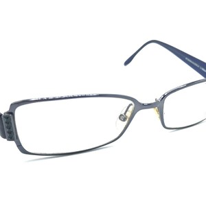 Puede incluir: Un par de gafas de metal negro con lentes transparentes. Las gafas tienen una forma rectangular y un fino marco de metal.