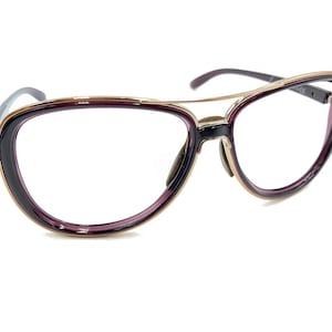 Könnte beinhalten: Eine Brille mit einem schwarzen und violetten Rahmen und goldenen Akzenten. Die Gläser sind klar.