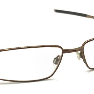 May include: Brown metal frame eyeglasses with clear lenses. The frame has a rectangular shape with a thin metal design.