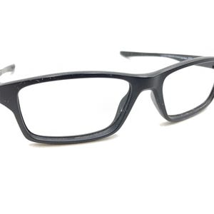 May include: Black rectangular eyeglasses with clear lenses. The frames are a matte black and have a modern, minimalist design. The glasses are set against a white background.