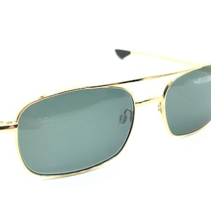 May include: Gold-framed sunglasses with green lenses. The sunglasses have a classic aviator style.