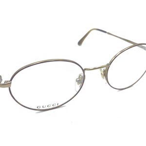May include: Gold-tone metal eyeglasses with round lenses and the word "GUCCI" printed on the frame.